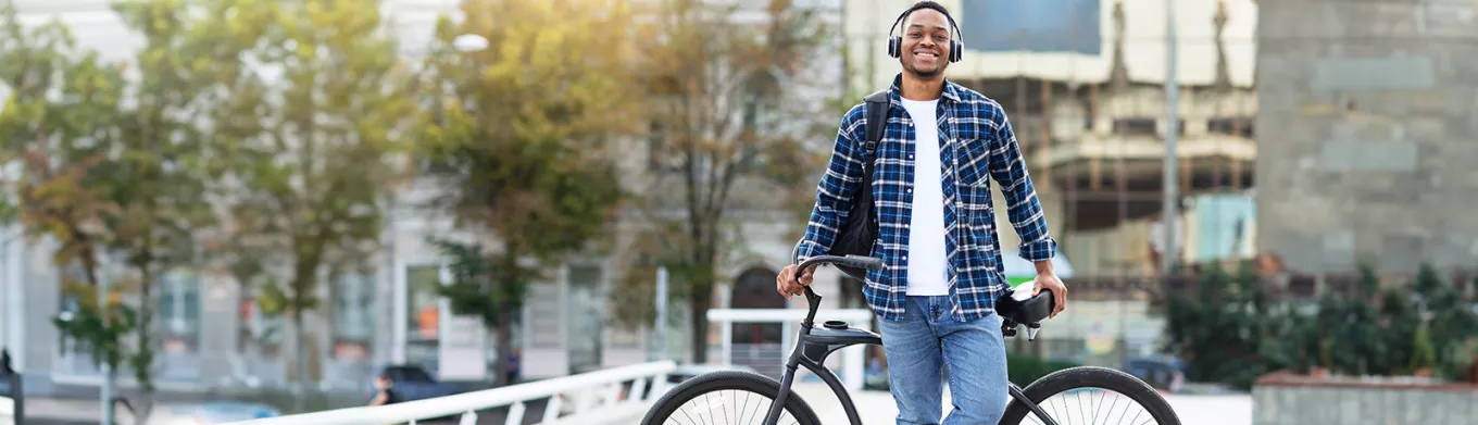 Smiling young man wearing headphones and leaning against his bike. 
