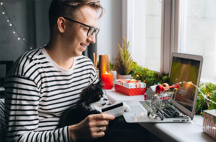 man sitting hat his laptop with a cat buying something - Christmas decorations