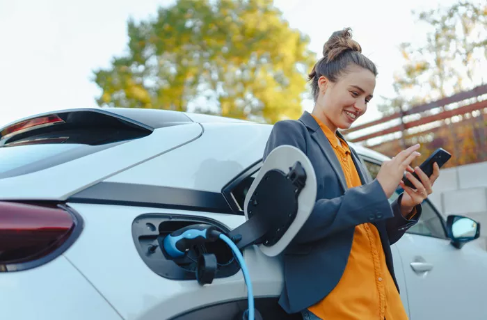 Woman standing by her electric car and using her phone while it charges