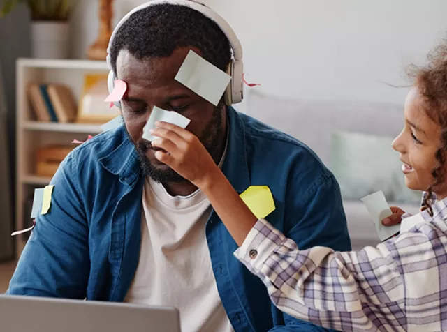 man working while child attaches sticky notes to his head