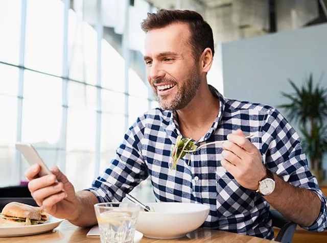 man eating food while reading from phone
