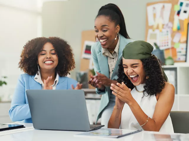 Three women by a laptop clapping their hands
