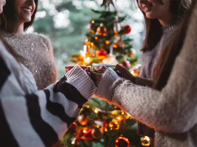 group of friends holding mugs around the Christmas tree