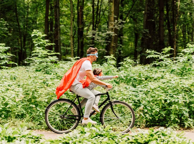 man riding a bike with son wearing a superhero cape