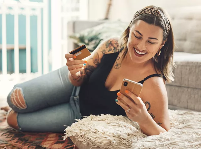 woman laying on a rug with her phone and bank card