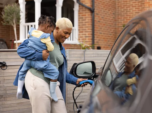woman holding her child and plugging in her electric car