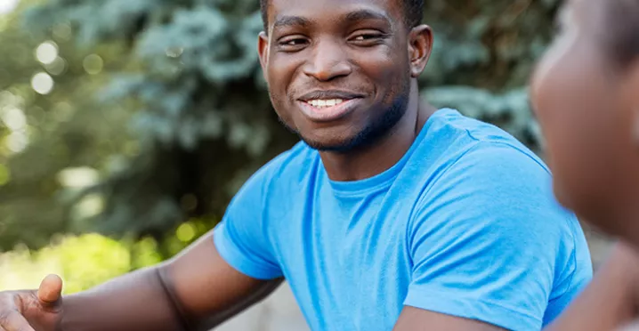 black man in blue shirt smiling during a conversation with a black woman.
