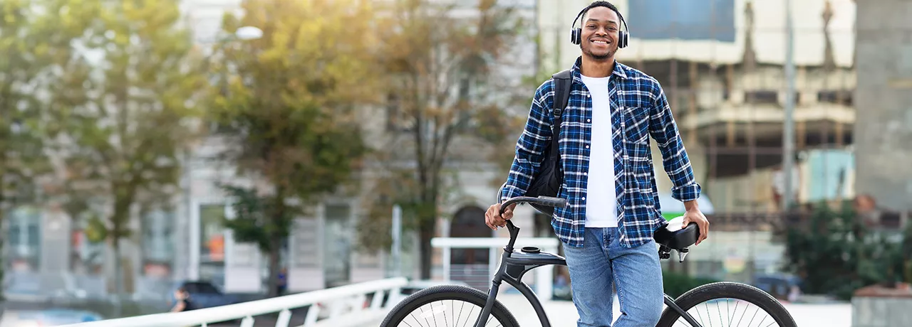 Smiling young man wearing headphones and leaning against his bike.