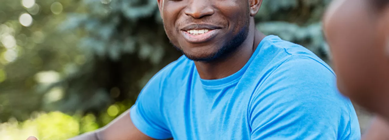 black man in blue shirt smiling during a conversation with a black woman.
