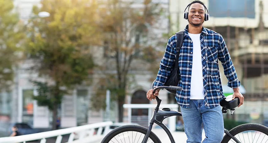 Smiling young man wearing headphones and leaning against his bike.