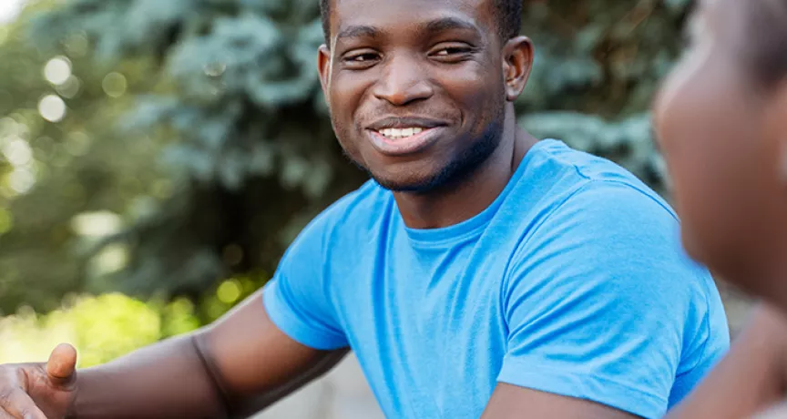 black man in blue shirt smiling during a conversation with a black woman.