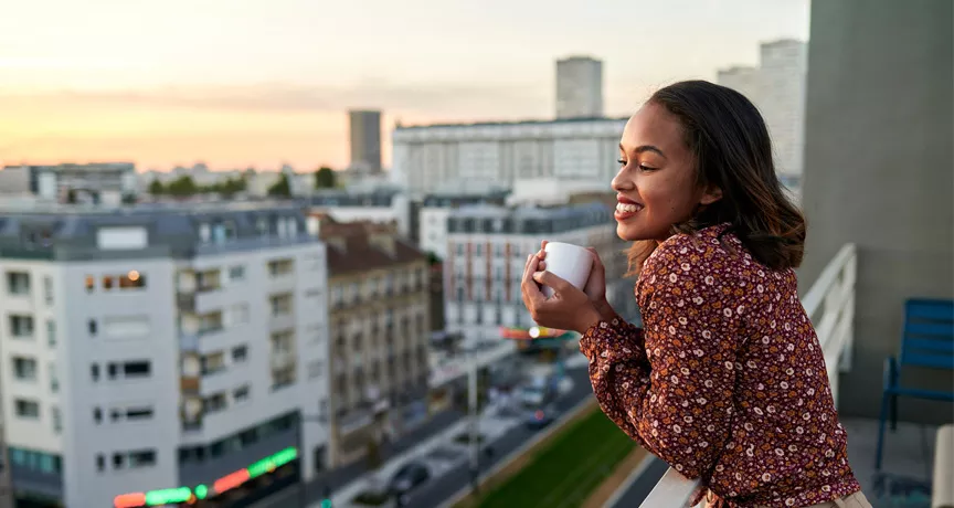 woman leaning over her balcony with a coffee