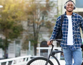 Smiling young man wearing headphones and leaning against his bike.