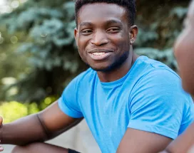 black man in blue shirt smiling during a conversation with a black woman.
