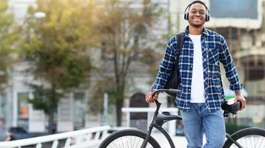 Smiling young man wearing headphones and leaning against his bike.