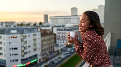 woman leaning over her balcony with a coffee